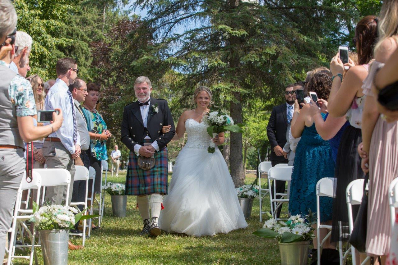 A father in a kilt walks his daughter down the aisle