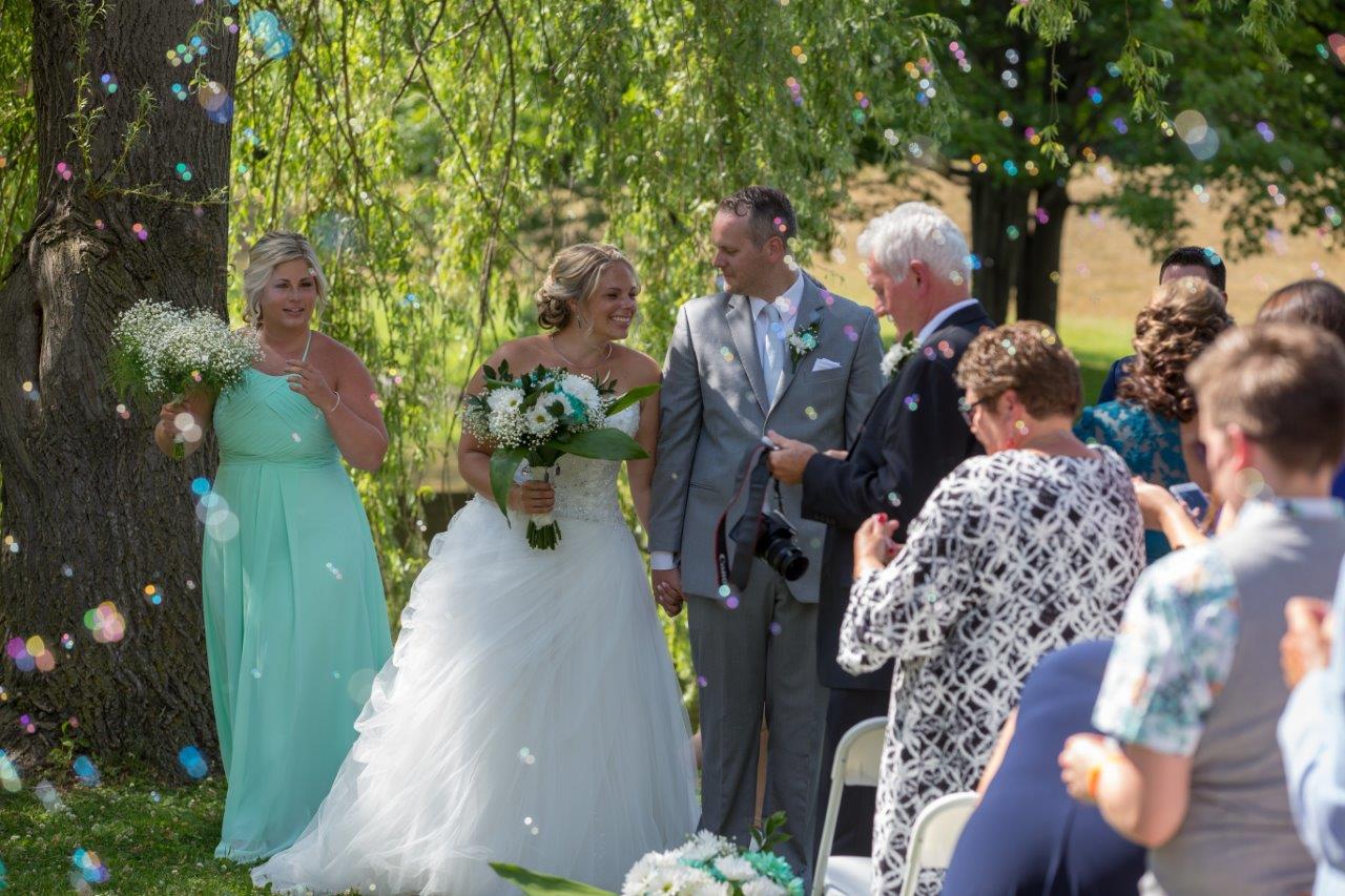 Bride and groom walk down the aisle with bubbles in the air