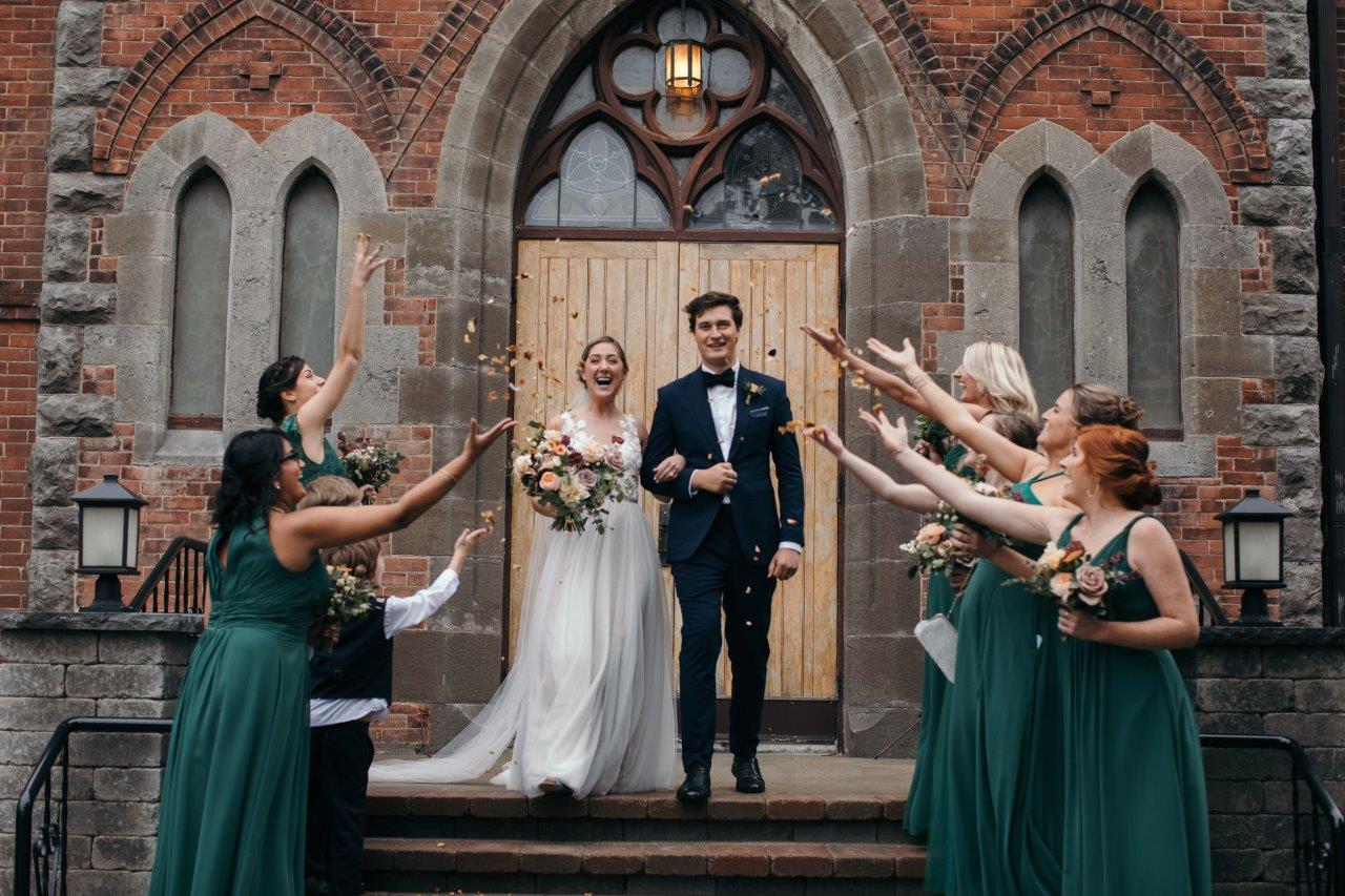 Bride and groom exit the church with confetti thrown by the bridesmaid
