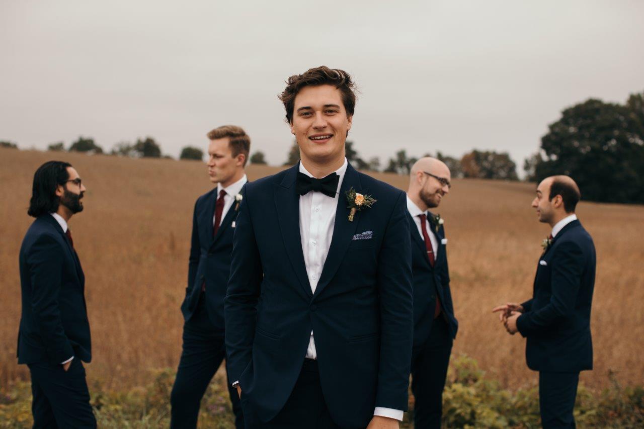 Groom walks towards camera with groomsmen in the background