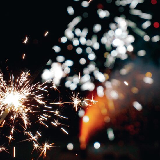 Close up of lighted sparkler with fireworks in the background