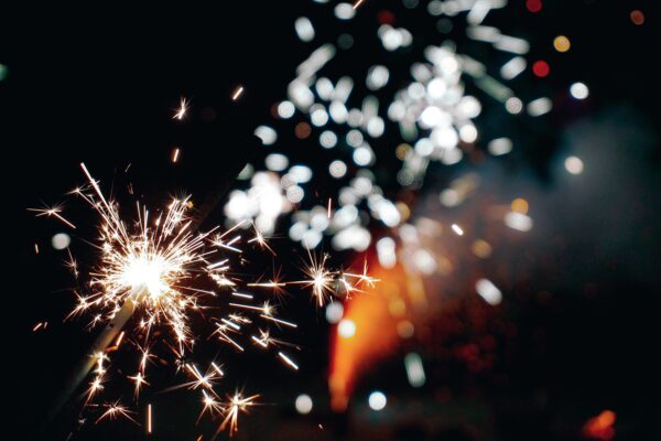 Close up of lighted sparkler with fireworks in the background