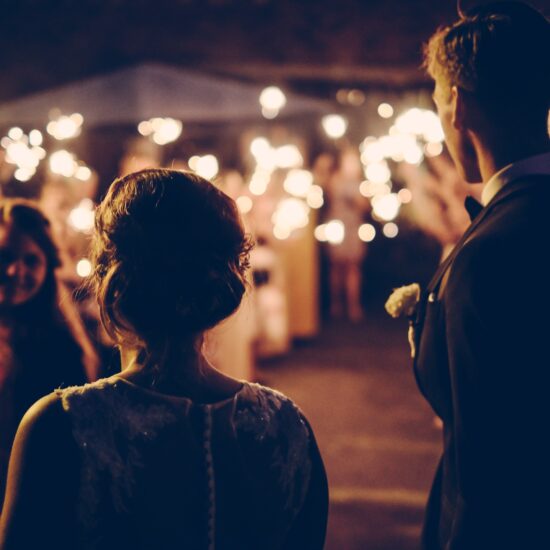 Two people look on at an outdoor nighttime wedding illuminated by sparklers.